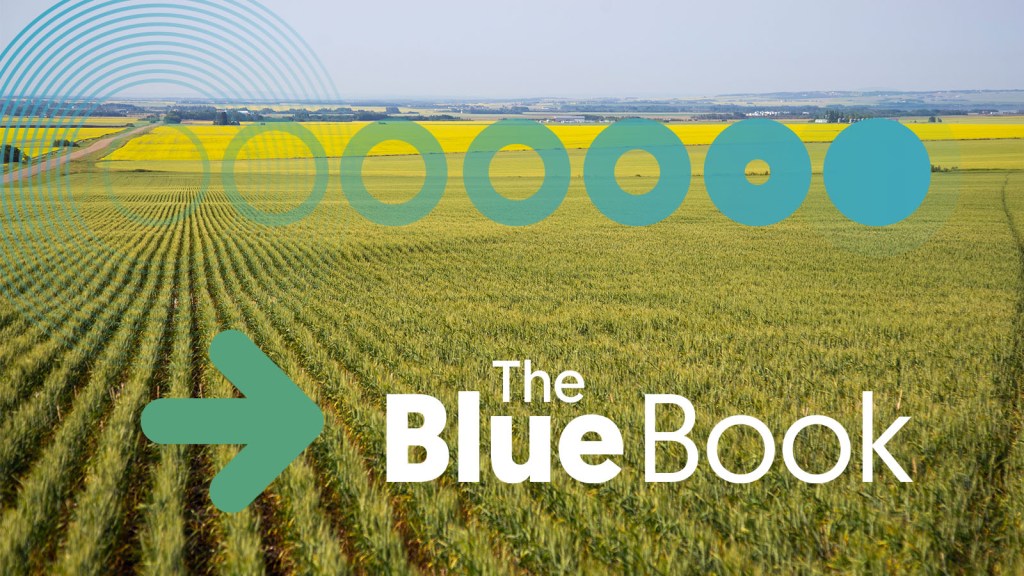 A panoramic view of a green agricultural field with a yellow canola field in the background and a clear sky. The text 'The Blue Book' is prominently displayed along with a directional arrow.